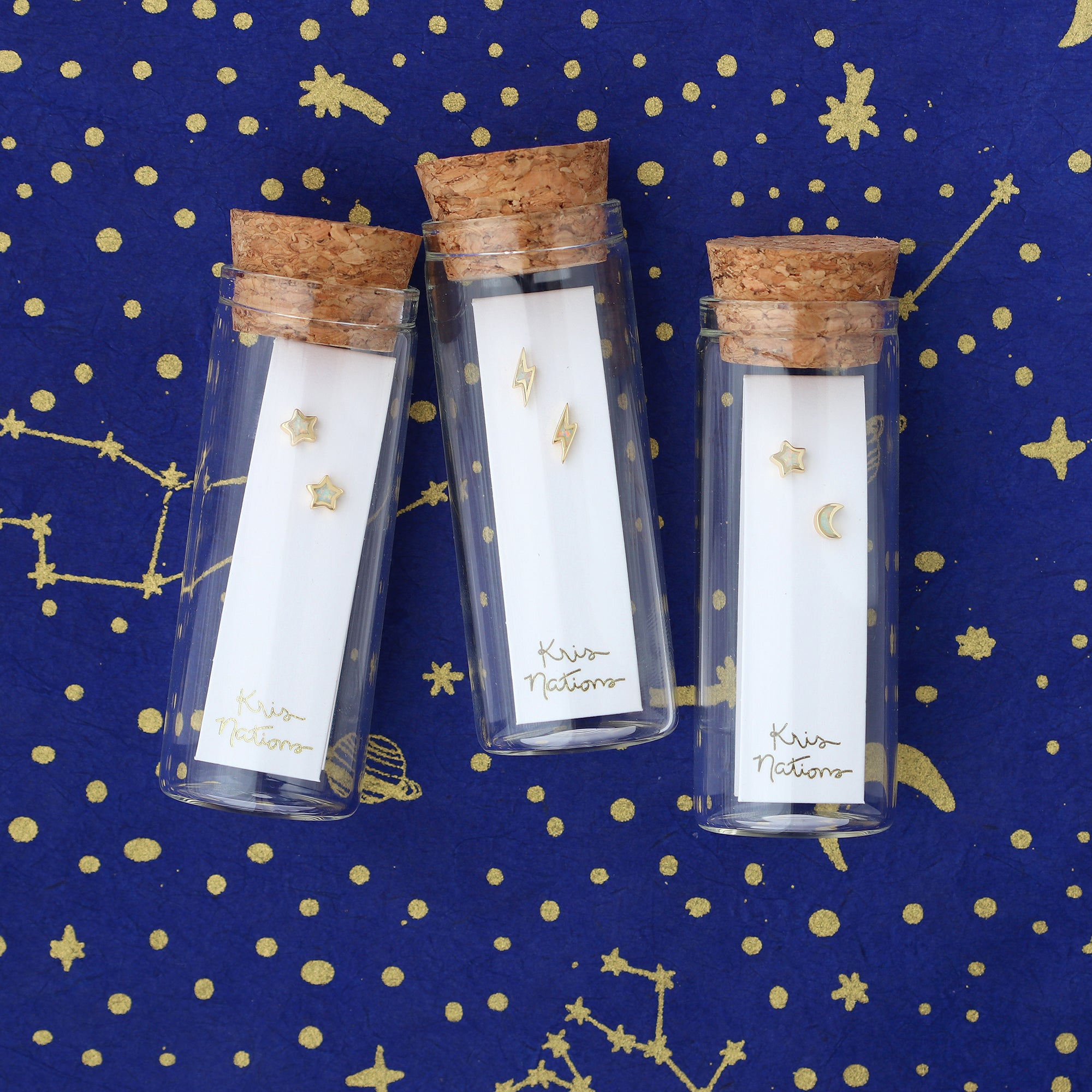 Three glass bottles with cork lids on a blue background with gold stars and constellations.